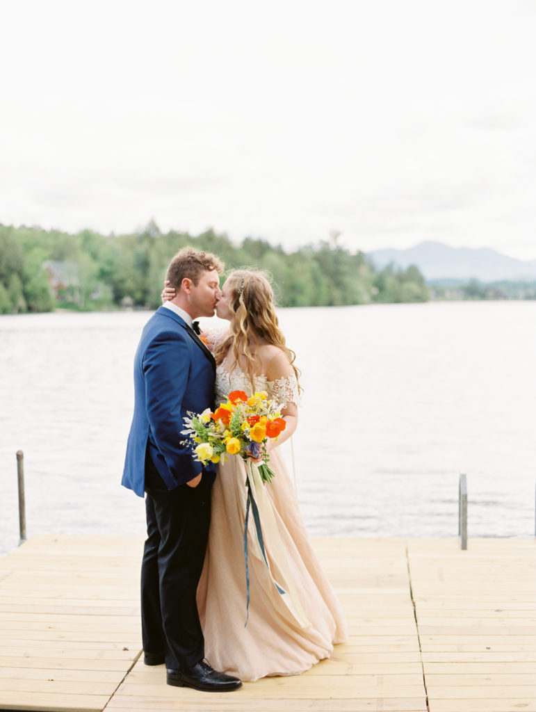 bride and groom kissing on the dock on wedding day with icelandic poppy bouquet | Mary Dougherty