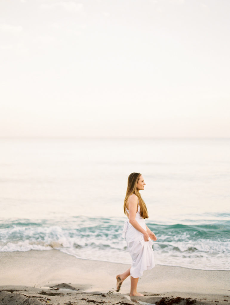 woman walking in white dress in bare feet on beach next to ocean