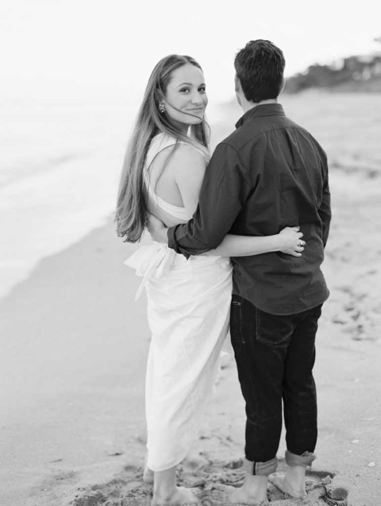 woman looking back standing next to fiance on beach