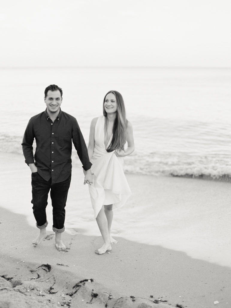 black and white engagement photo of couple walking away from ocean laughing and happy | Mary Dougherty