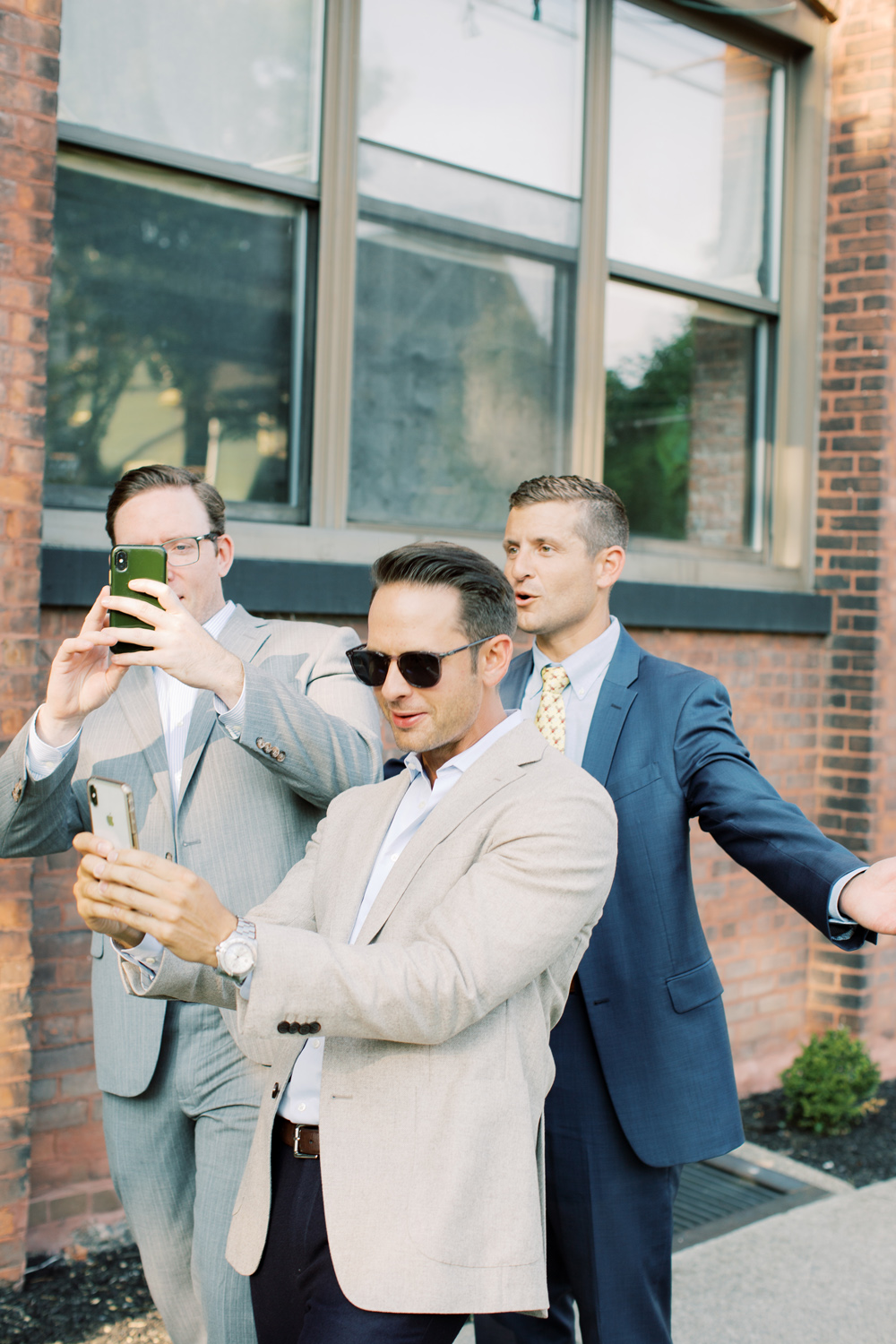 group of three guys take photos on phone during wedding weekend