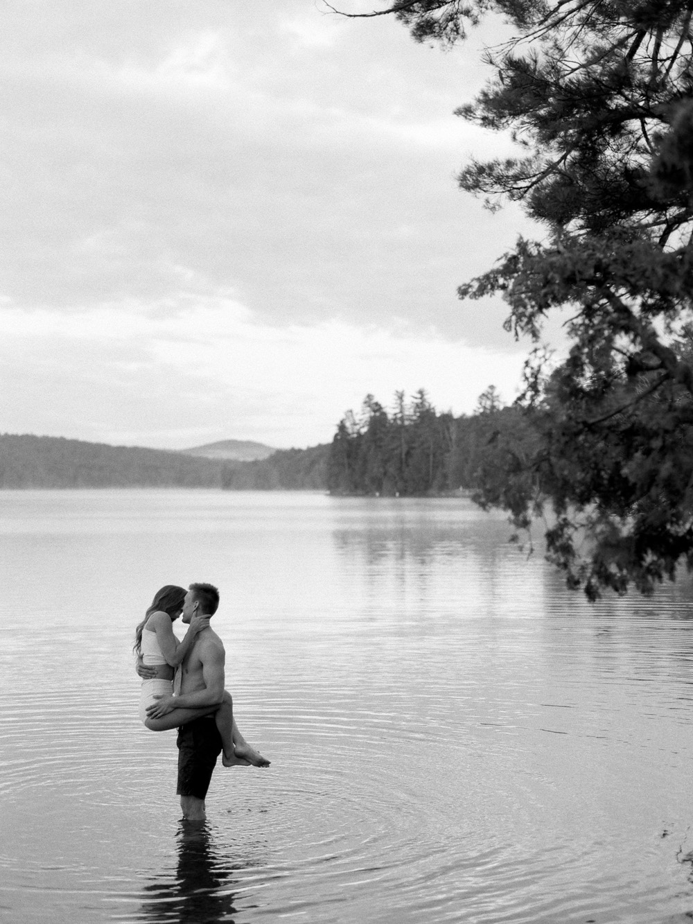 guy holding girl in water kissing in Adirondacks on honeymoon in lake Mary Dougherty