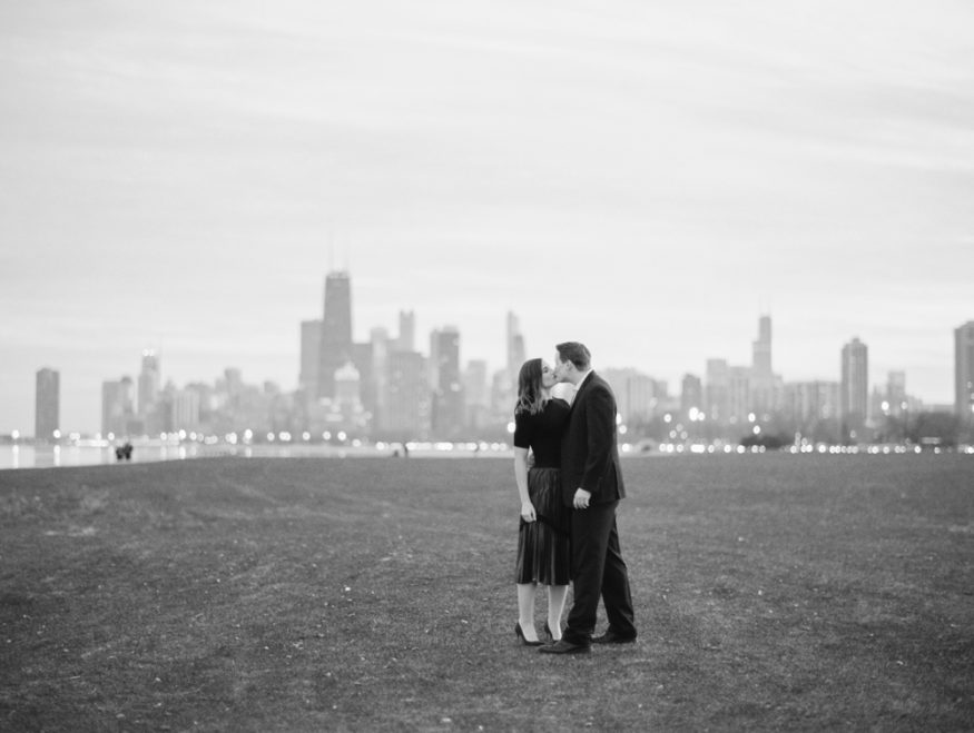 portrait of a man and woman kissing with Chicago skyline city in the background engagement photo on bw film by Mary Dougherty