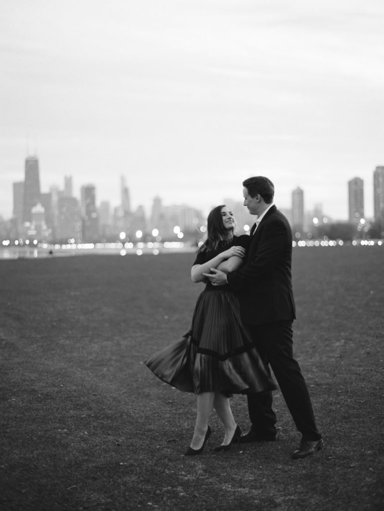 couple dances and twirls into dip in Chicago with city skyline in distance at night engaged by Mary Dougherty