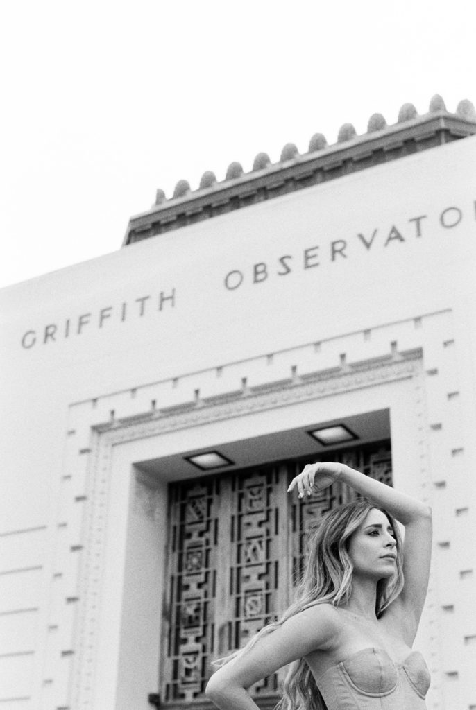 woman stands in front of Griffith Observatory in bw photo gazes out to hollywood sign Mary Dougherty