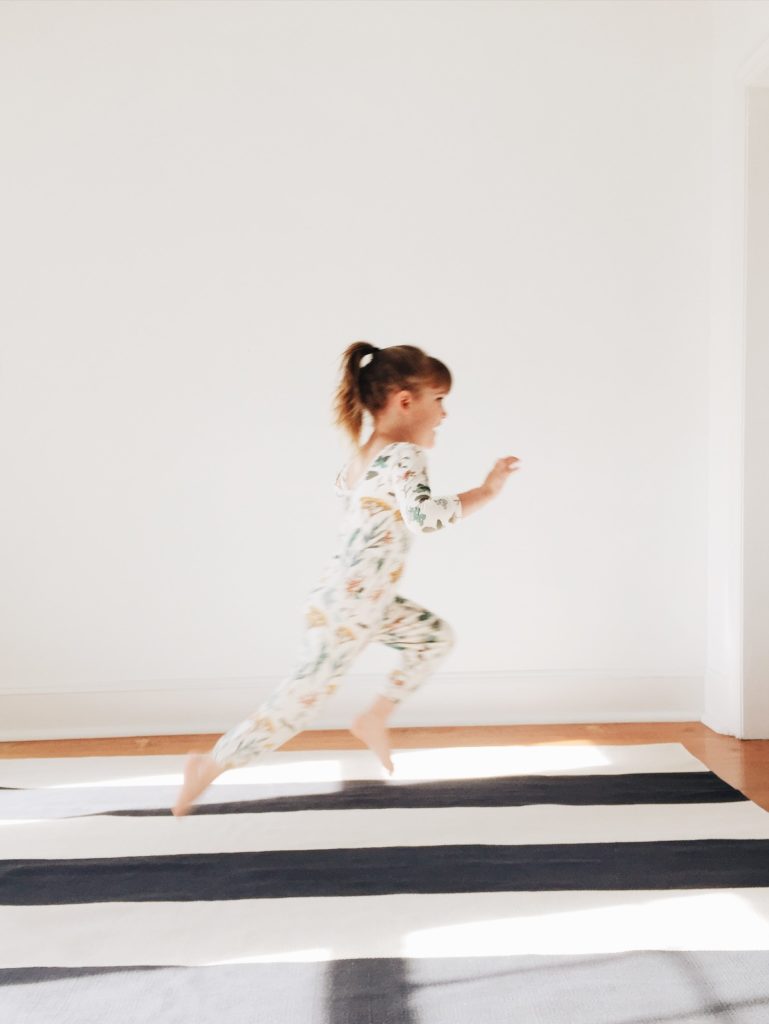 little girl runs in alice + ames floral jumpsuit on striped west elm rug in white bedroom | iphone photography by Mary Dougherty