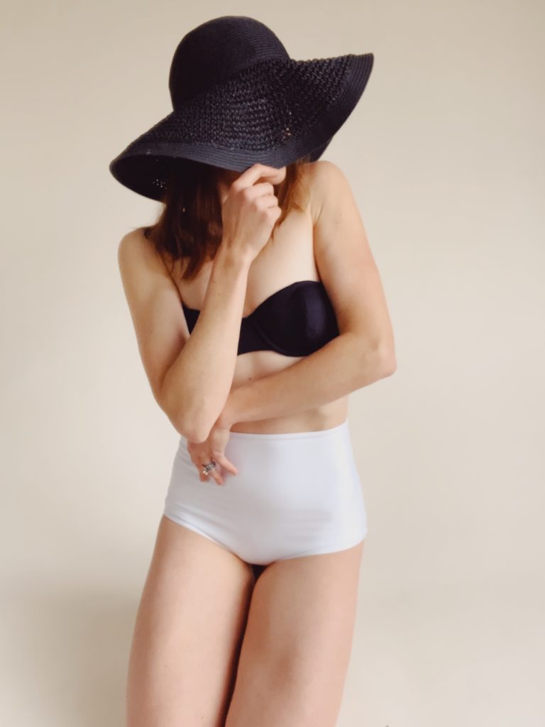 self portrait of woman in bathing suit with black straw hat in home studio
