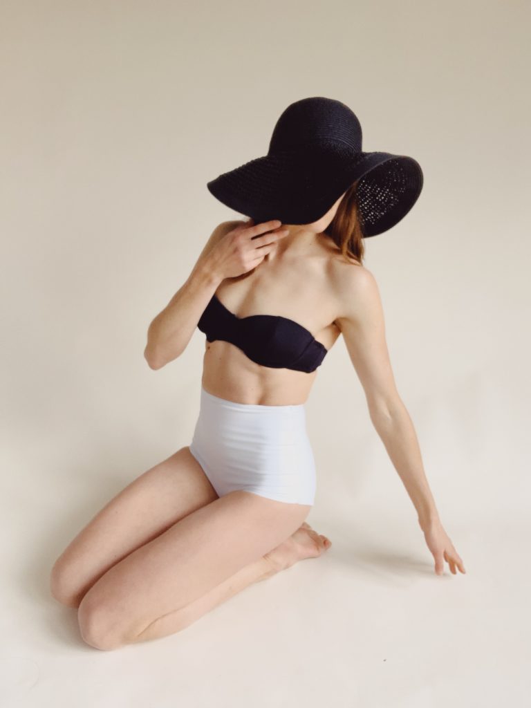 self portrait of woman in bathing suit with black straw hat in home studio with seamless paper