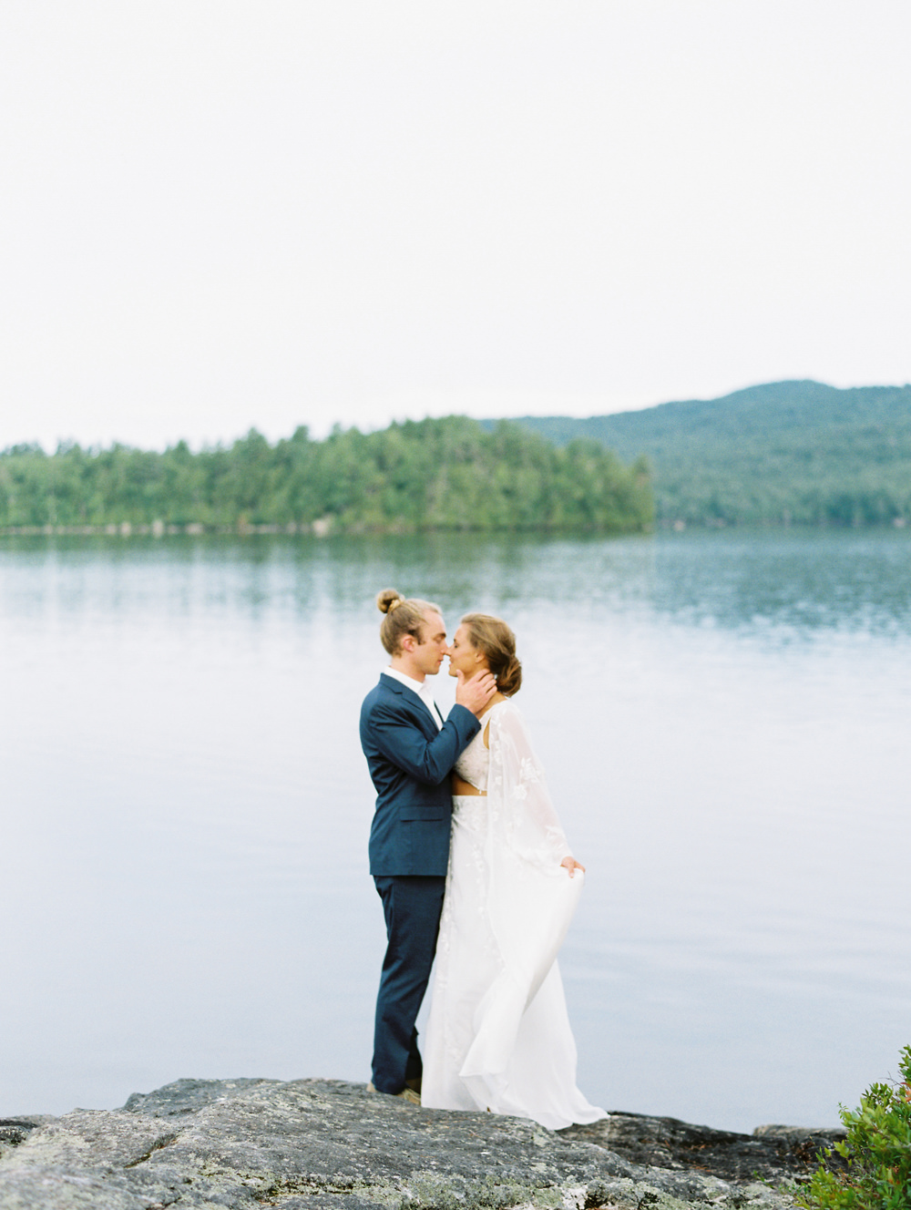 bride and groom stand for kiss on waters edge in Adirondack Island Elopement by Mary Dougherty