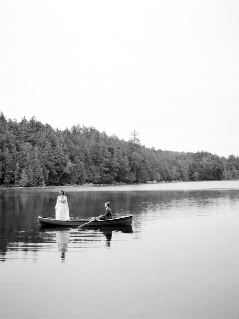 bw photo of couple in boat paddling bride standing looking towards lake in Adirondacks by Mary Dougherty