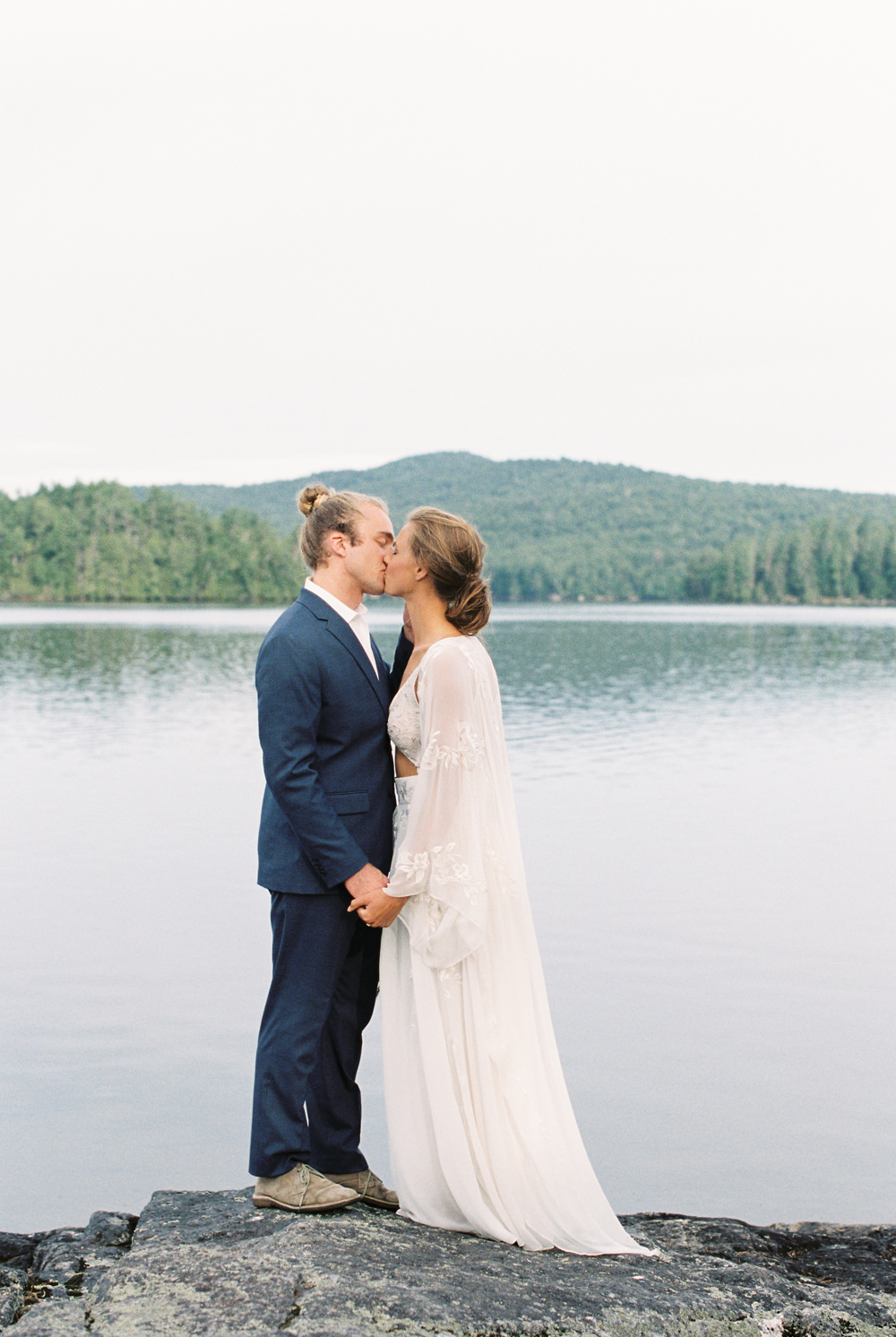 bride and groom kiss standing on rock with lake behind them in Adirondack Wedding Workshop | Island Elopement by Mary Dougherty