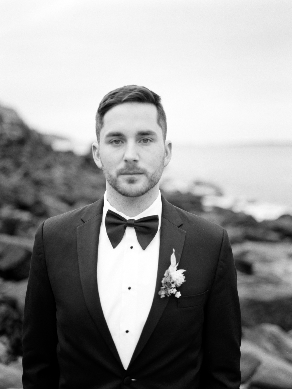 groom stands on beach looks at camera in bw film photo Portland Maine elopement | Mary Dougherty
