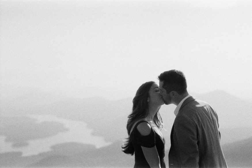 black and white photo of couple kissing on top of a mountain with view behind them | Mary Dougherty