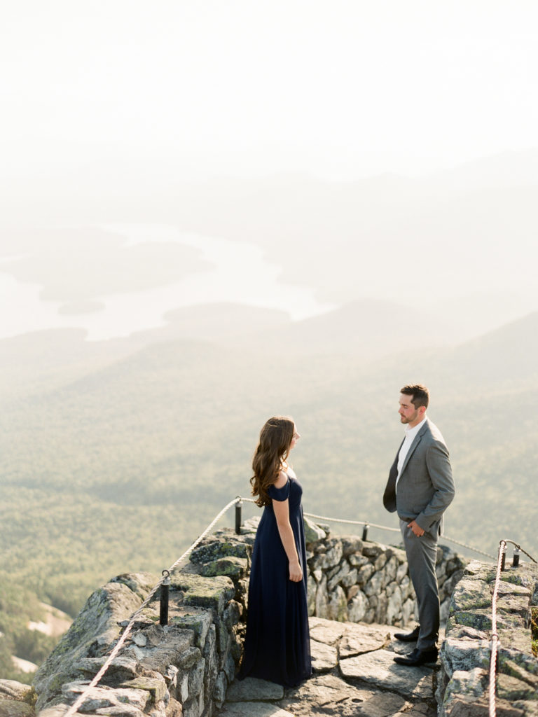 dressed up couple stands on rocky steps with mountain landscape during Adirondack engagement session | Mary Dougherty