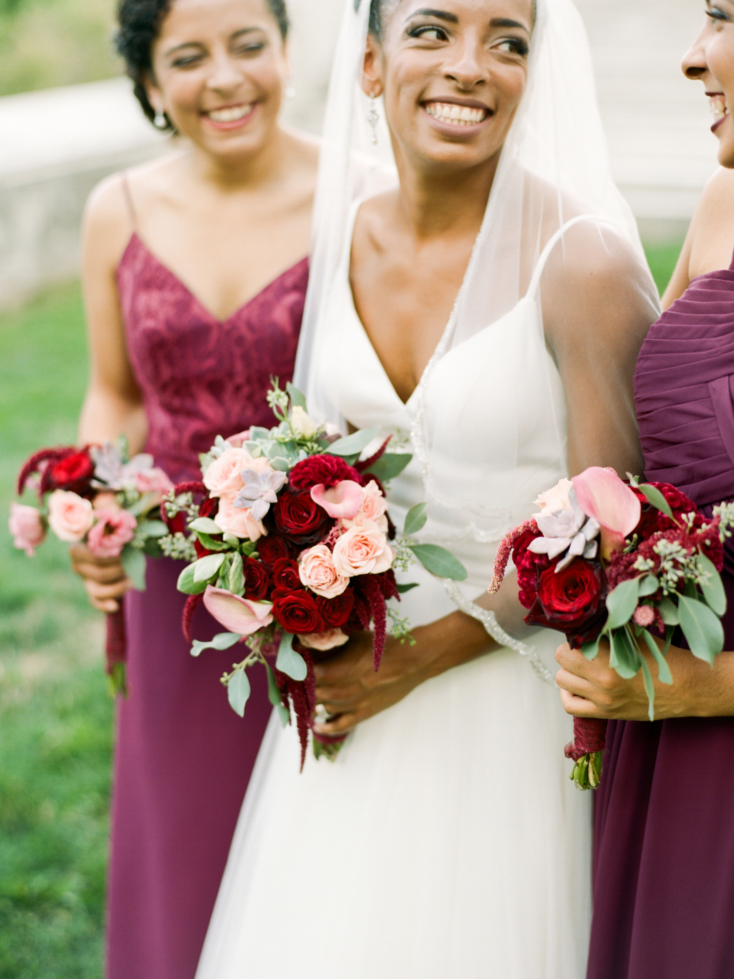 Happy bride with bouquet stands with bridesmaid in maroon dresses and rose and calla lily bouquets | Mary Dougherty Photography