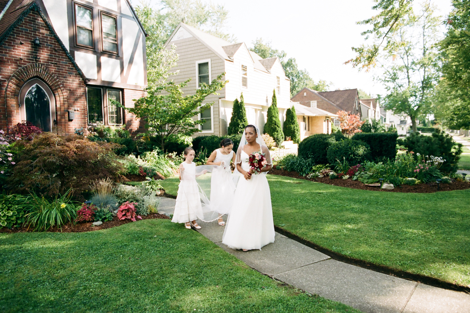 Backyard Wedding | Bride walks out front door of home with flower girls holding veil | photograph by Mary Dougherty