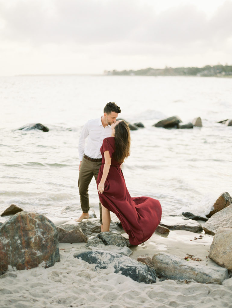 Bride-to-be in gorgeous red dress kissing future husband in engagement photos on the beach | Mary Dougherty destination film wedding photographer