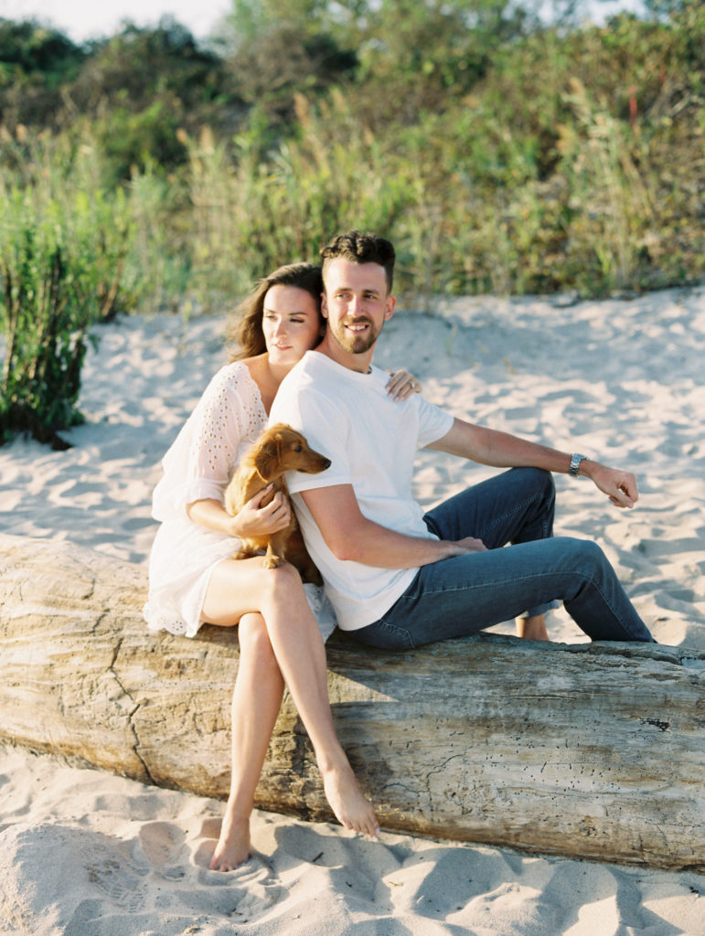 Couple sitting on fallen tree in the sand with their Dachshund
