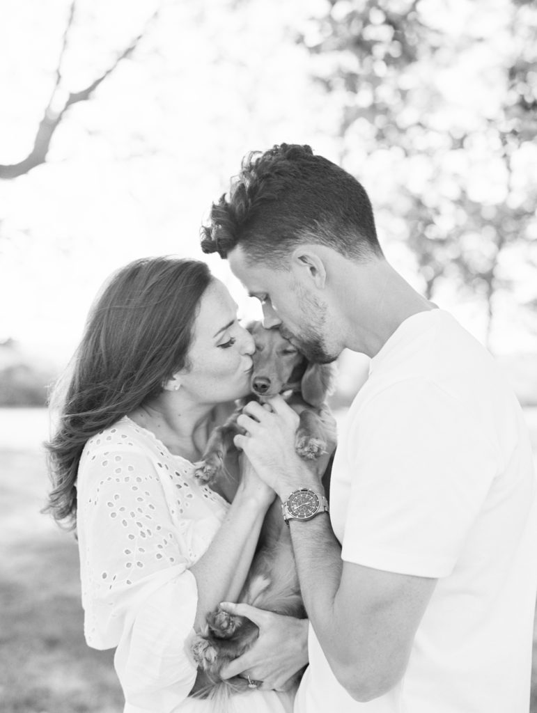 Black and white photo of couple snuggling their dog during a beach engagement photoshoot