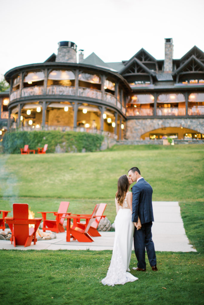 Bride and Groom stand in front of Lake Placid Lodge at night on wedding day kissing | Intimate wedding in the Adirondacks photographed by Mary Dougherty