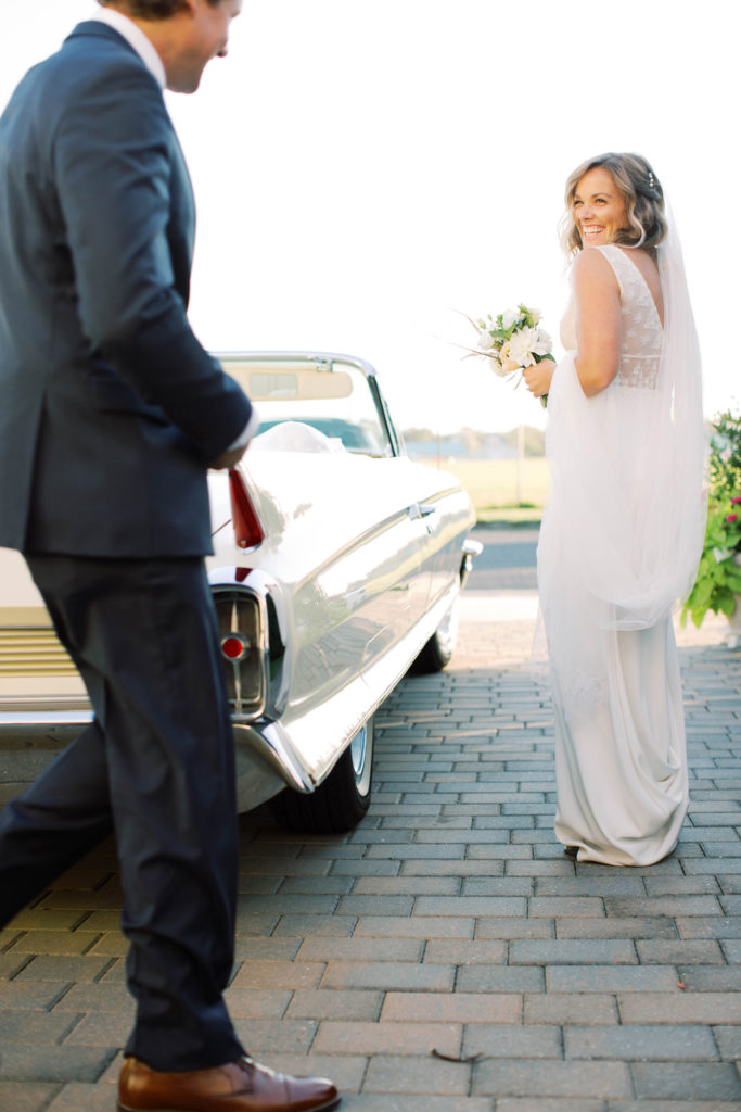 bride and groom smile at each other walking towards Cadillac in candid wedding photo by Mary Dougherty