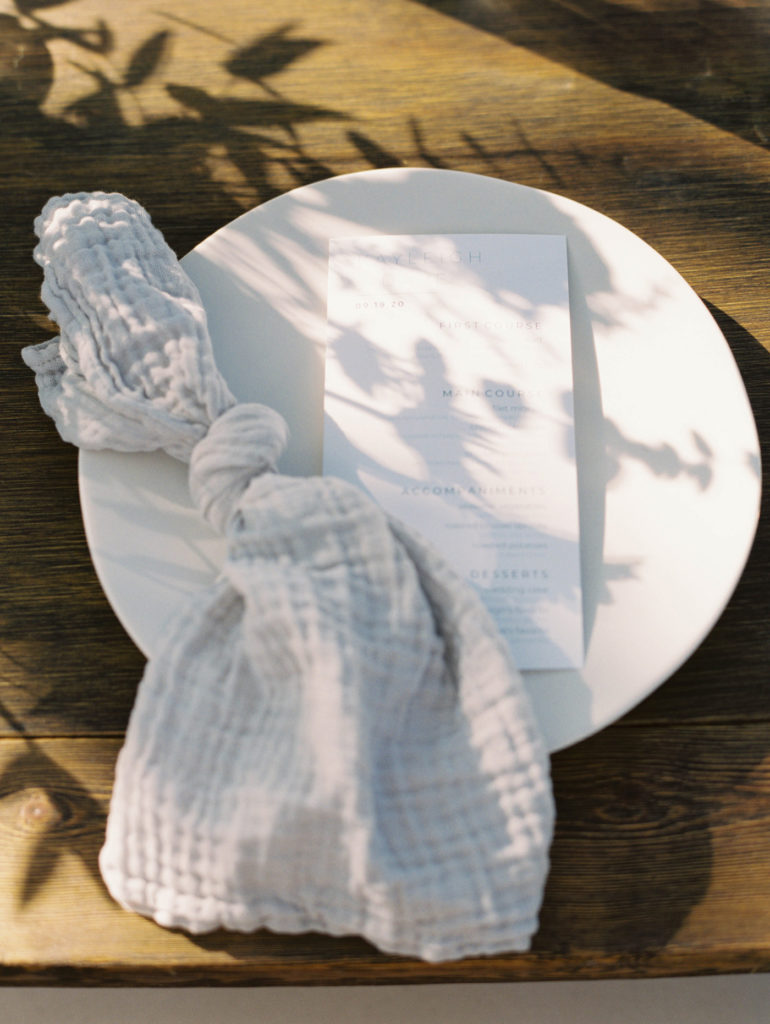 Flowers cast shadow on place setting at farmhouse table for backyard wedding photographed by Mary Dougherty