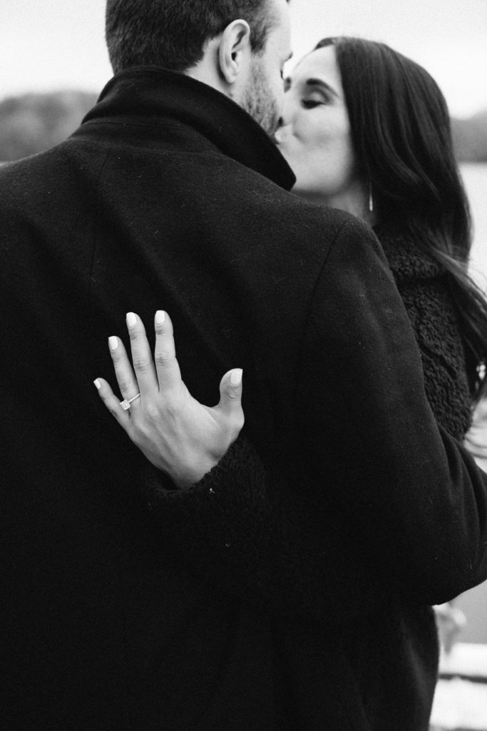 black and white photo of couple kissing with back to camera and engagement ring on hand