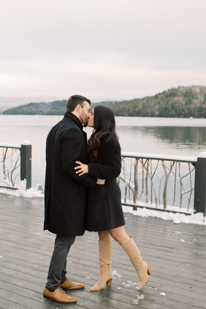 couple kisses on the dock at the lake placid lodge in the winter 