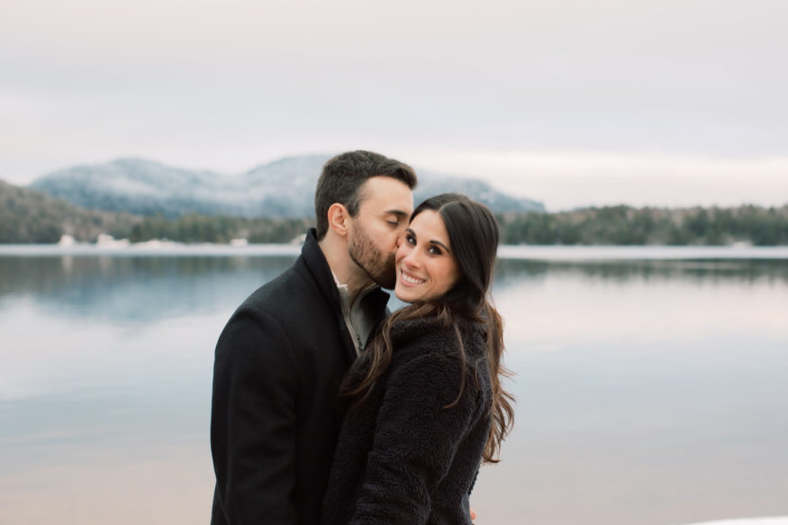 woman looks at camera while man kisses cheek | just engaged at the Lake Placid Lodge by Mary Dougherty