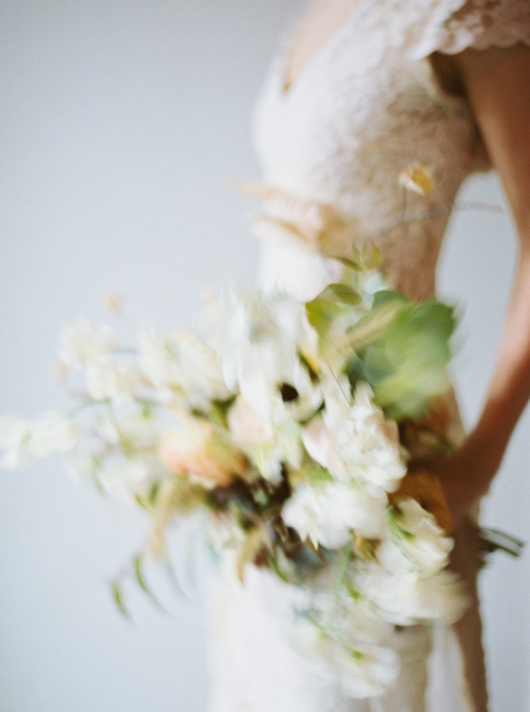 blurry bridal bouquet in white, cream, green and gold for a Catskills winter elopement photo by Mary Dougherty