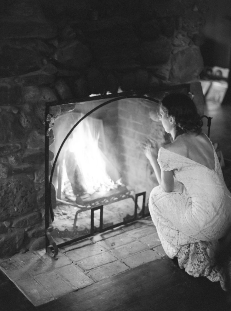 bride gets warm by the fire at foxfire mountain house during her Catskills winter elopement photo by Mary Dougherty