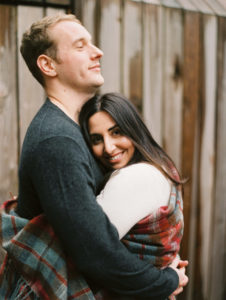 couple embraces and looks happy with plaid blanket at Gather Greene Catskills wedding venue image by Mary Dougherty