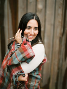 woman with dark hair looks away from the camera with a plaid blanket cozy around her