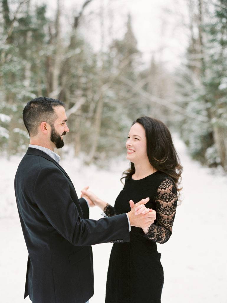 couple holds hands and smiles while dressed elegantly outside in the snow