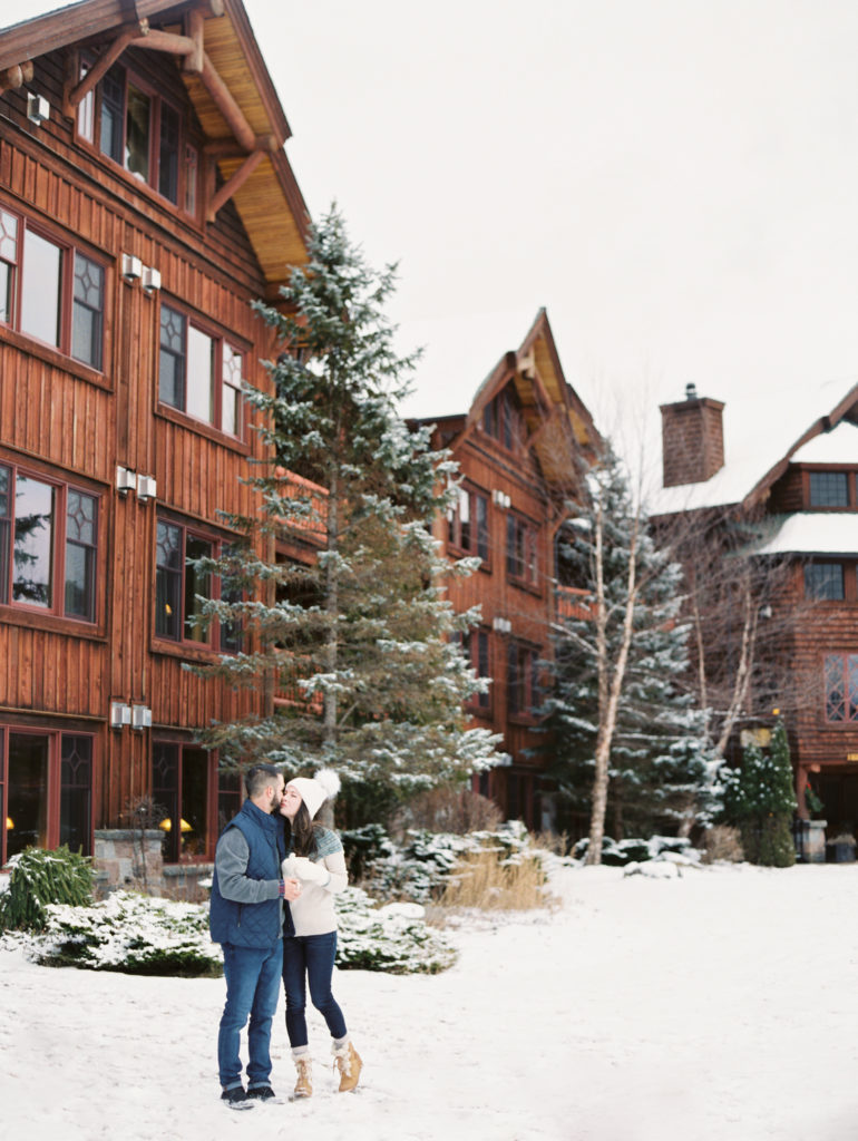 Engagement photo at the Whiteface Lodge in winter couple stands outside in snow and kisses