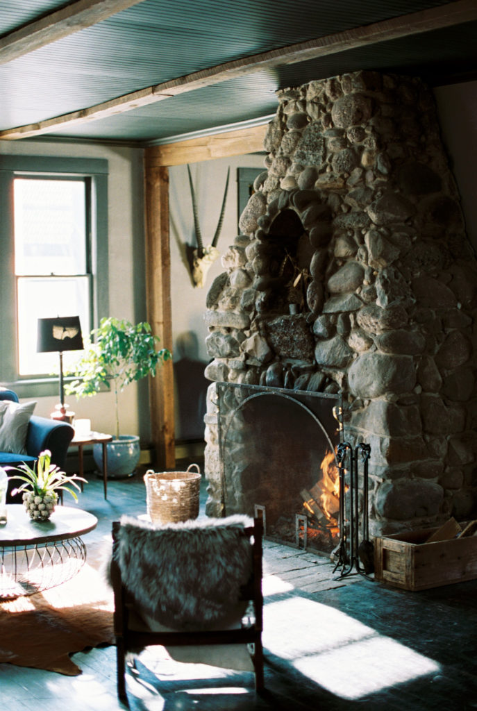 Living room with large stone fireplace in moody Catskills retreat | Mary Dougherty