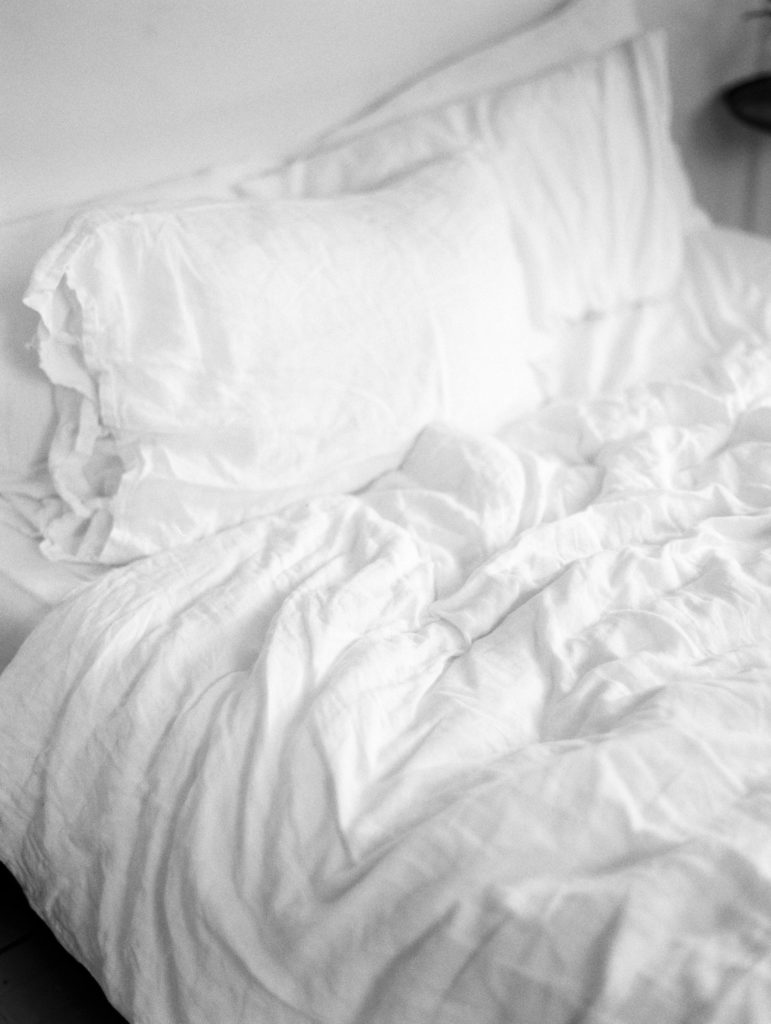 black and white photo of unmade bed with linen sheets rumpled romantic catskills getaway | branding session for Foxfire Mountain House photographed by Mary Dougherty