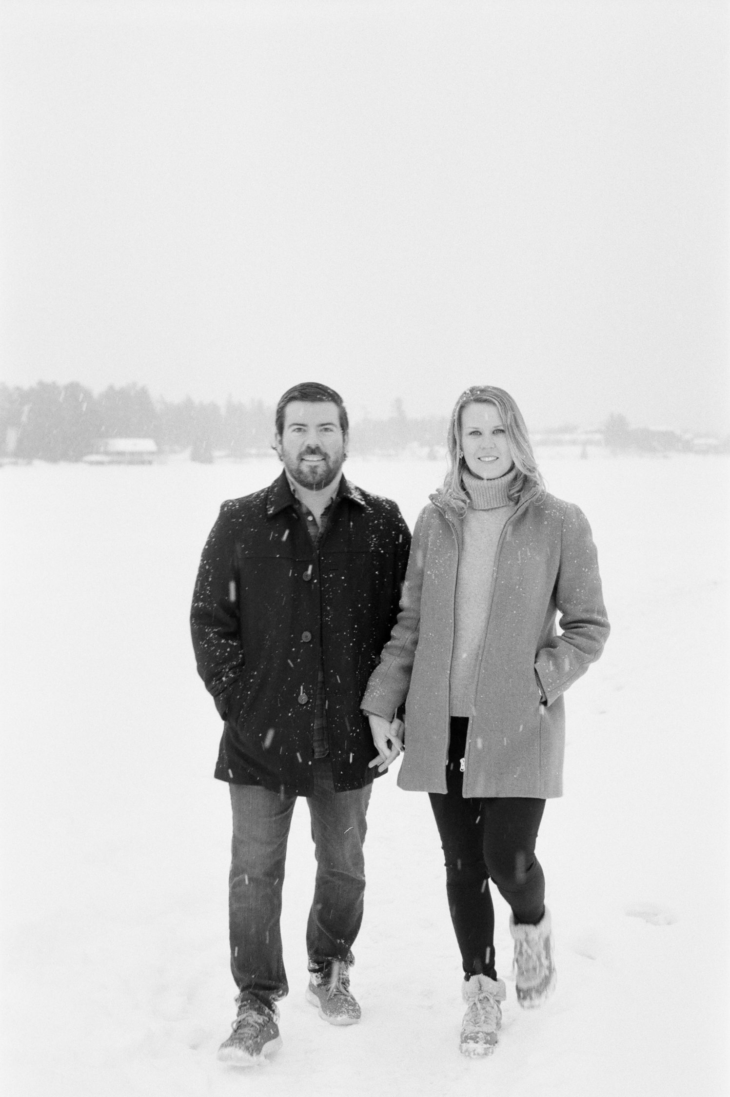 black and white photograph of couple holding hands standing in a snowy scene in Lake Placid on Mirror Lake. Photograph by Mary Dougherty