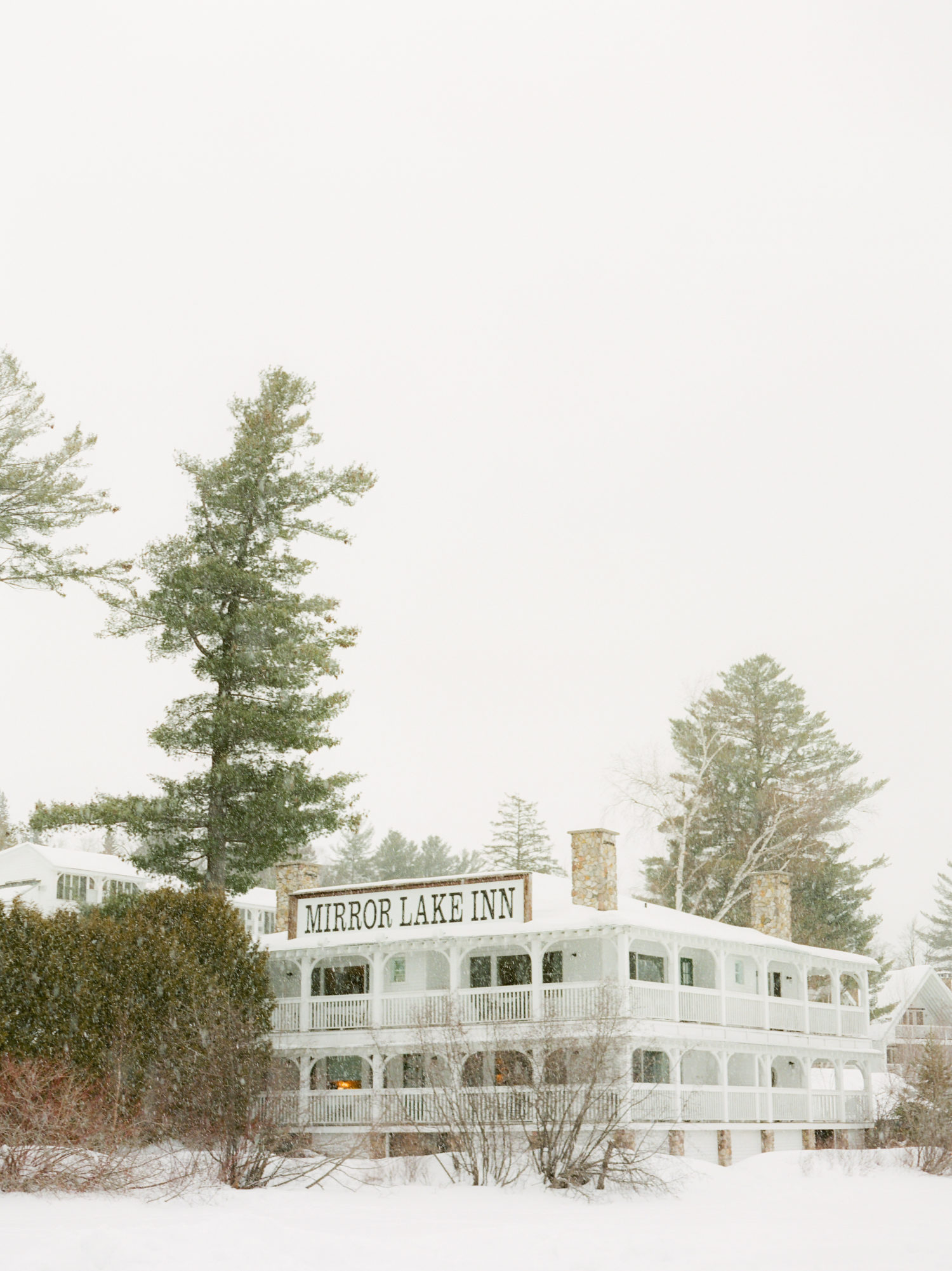 Mirror Lake Inn with snow falling photographed from the frozen lake during winter. Photograph by Mary Dougherty
