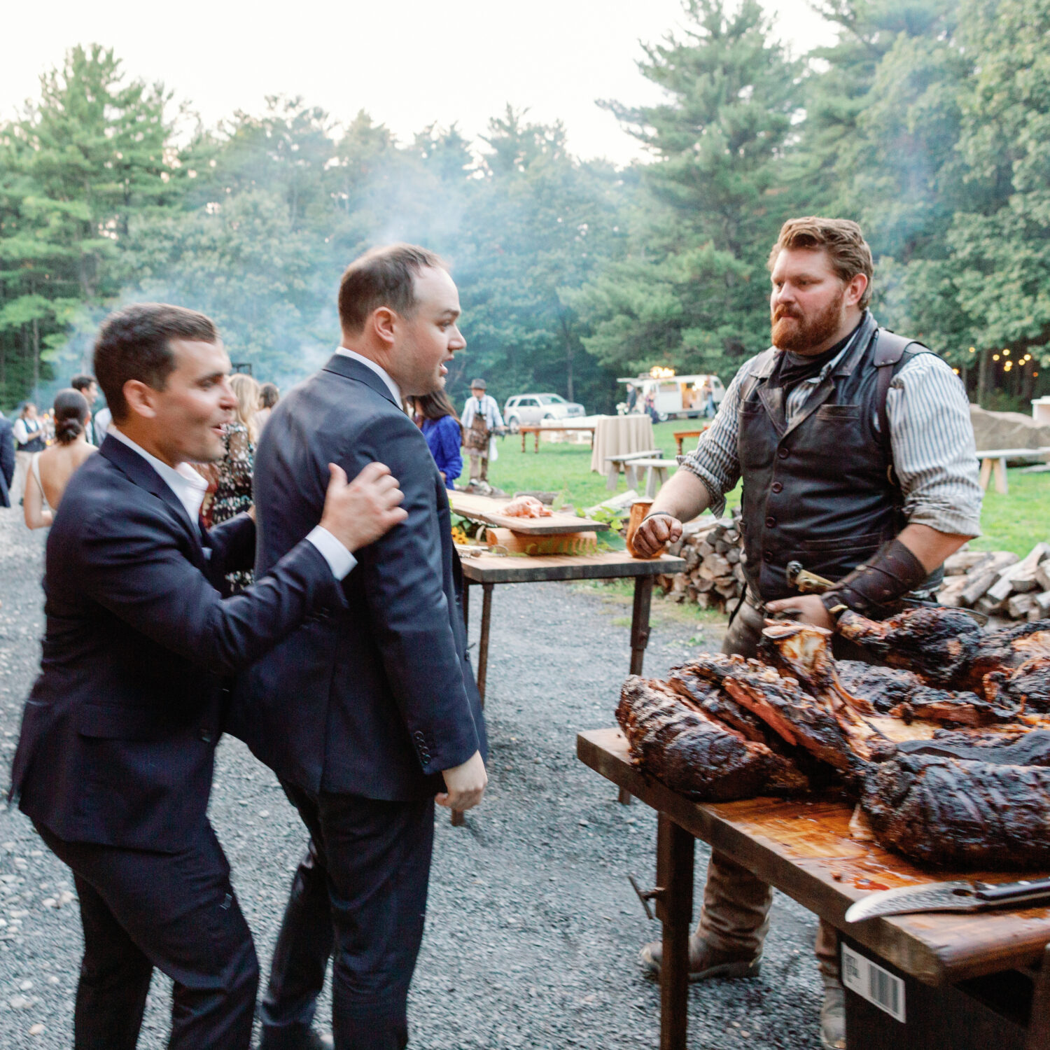 Groom is pumped up by friend as he approaches table of food catered by Heirloom Fire on wedding day at Gather Greene.