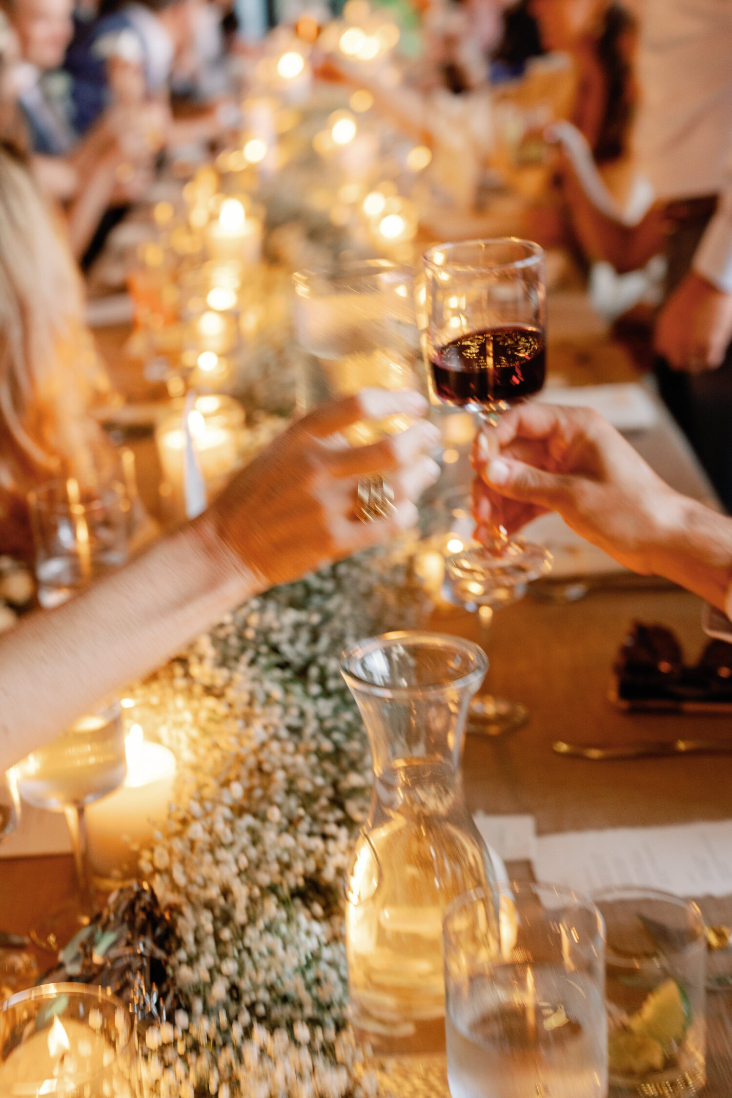 Image of a candlelit reception table with glasses clinking to cheers in the center, slightly blurred with the feeling of motion
