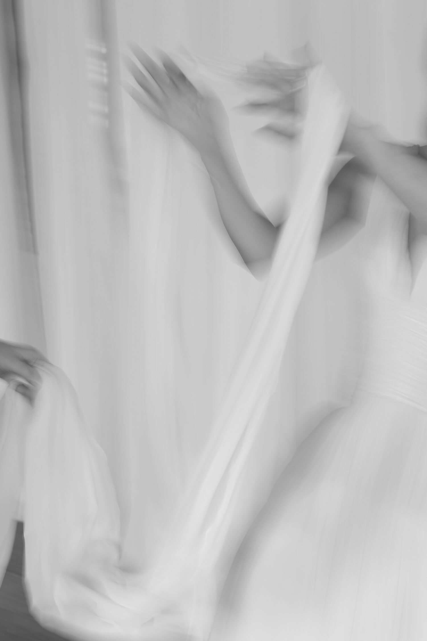 blurry bw photo of a bride putting a neck scarf on while dressing in her Rime Arodaky gown